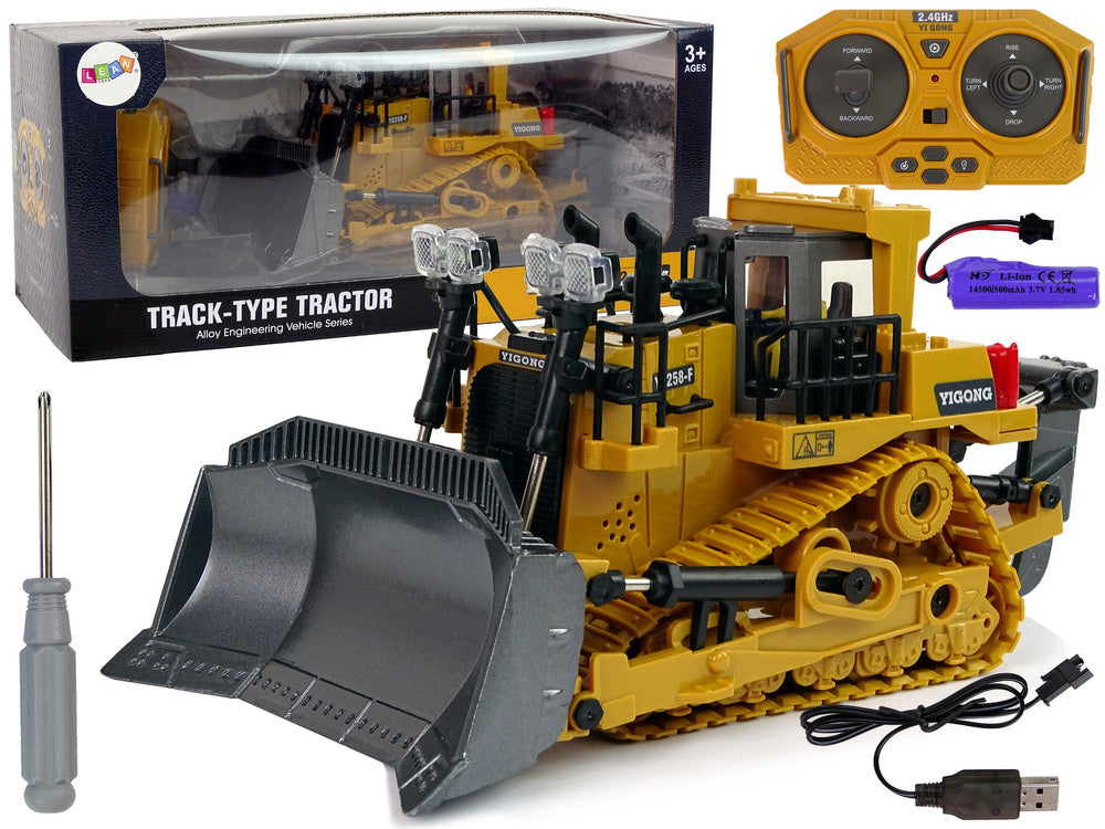 Rotaļu kāpurķēžu buldozers ar tālvadības pulti, akumulatoru un USB kabeli, izstādīts kopā ar iepakojumu.