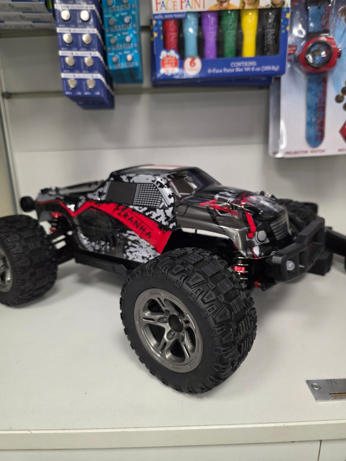 “RC mašīna Titan-X sānskats ar lielajiem bezceļa riteņiem un sarkanu grafiku