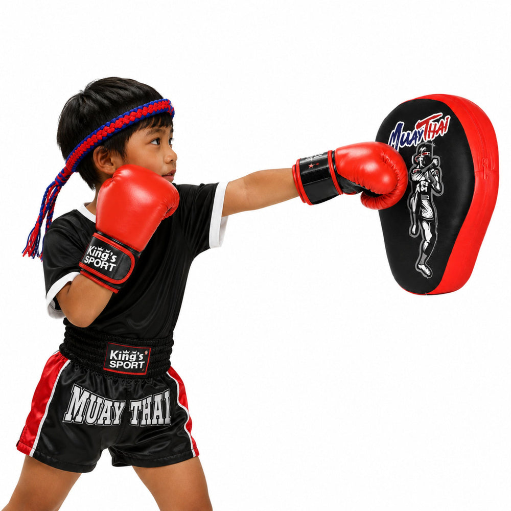 Bērns trenē sitienus ar sarkaniem boksa cimdiem un Muay Thai treniņu ķepu