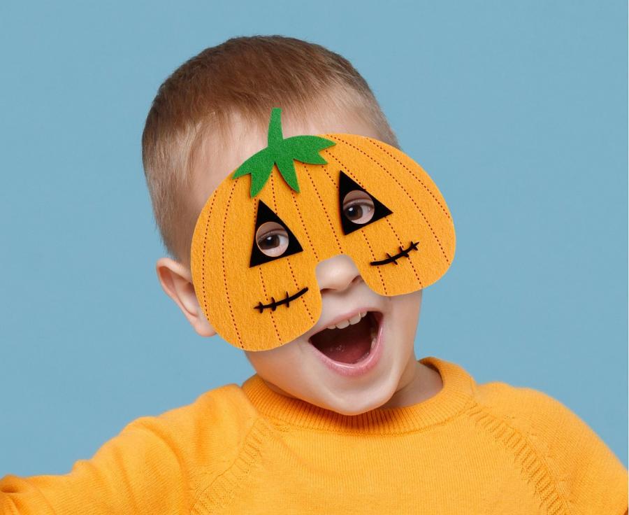 Bērns ar oranžu ķirbja formas filca masku sejā tuvplānā
