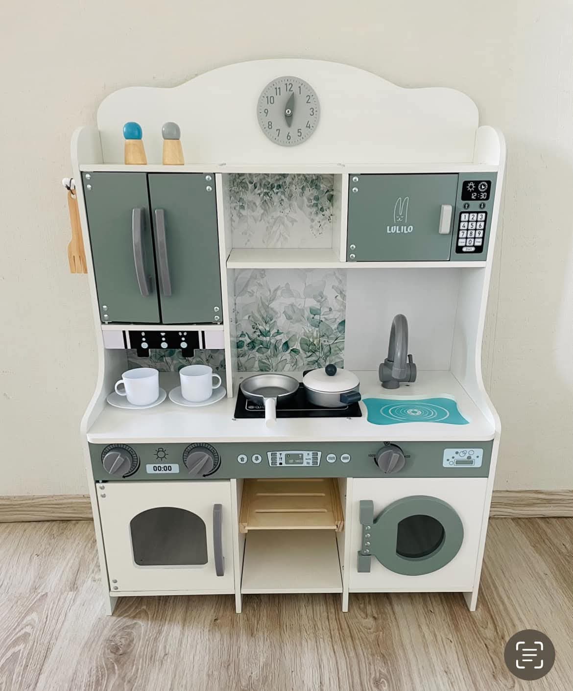 Koka rotaļu virtuve zaļpelēkos toņos ar plīti, izlietni, skapīšiem un trauku komplektu.