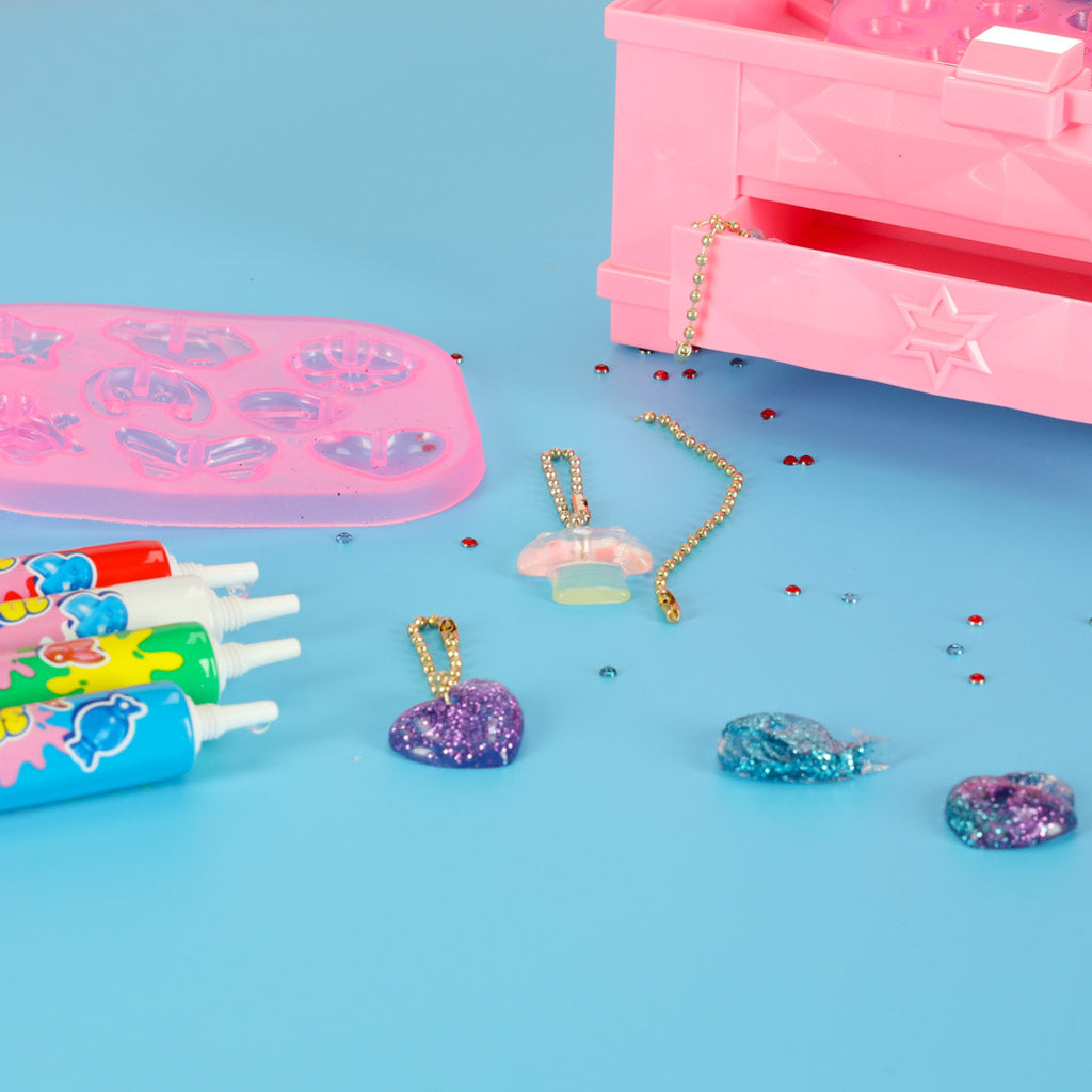 Magic Box komplekta gatavie piekariņi, veidnes un UV līmes tūbiņas uz zilas virsmas pie rozā kastes