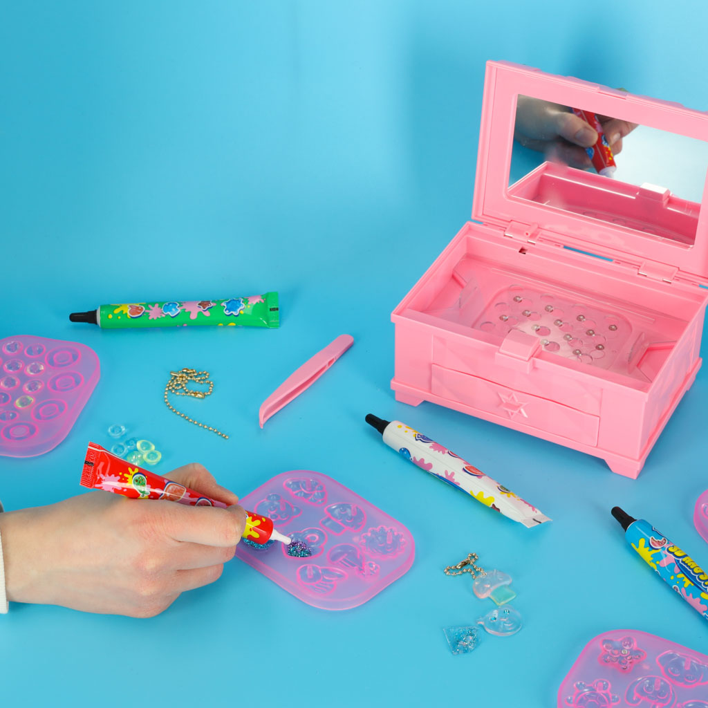 Bērns iepilda krāsaino UV gēlu Magic Box komplekta silikona veidnēs pie atvērtas rozā kastes.