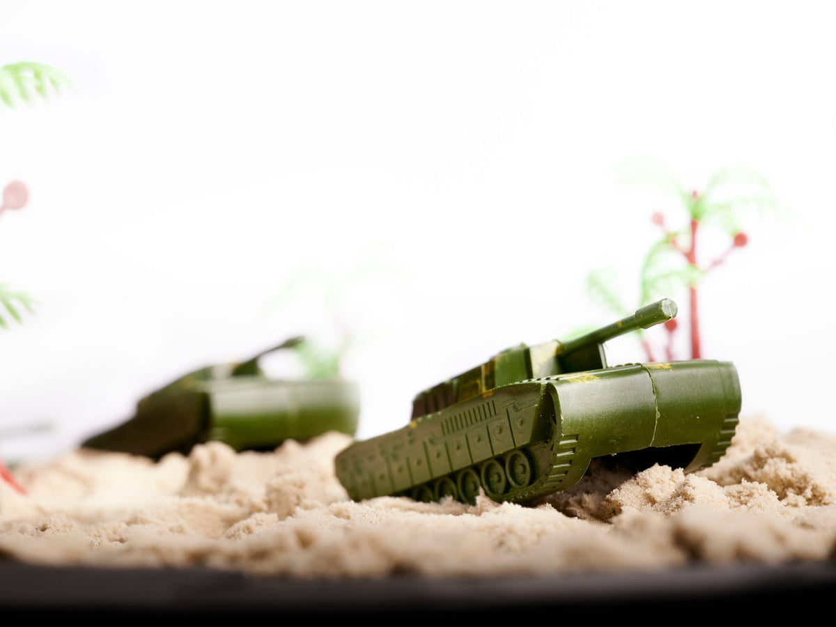 Militārais rotaļu tanks zaļā krāsā smilšu kaujas ainā