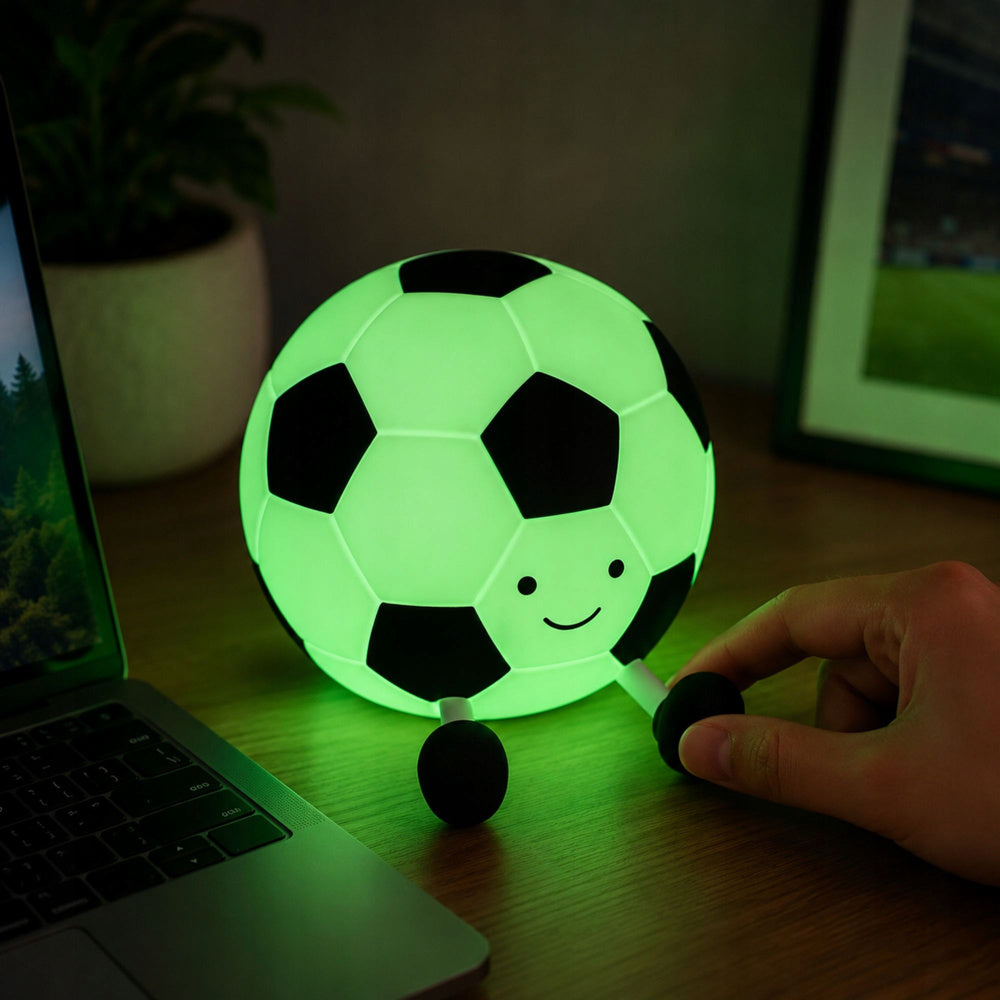 Mīksta silikona futbola bumbas LED RGB naktslampiņa zaļā gaismā uz galda blakus datoram