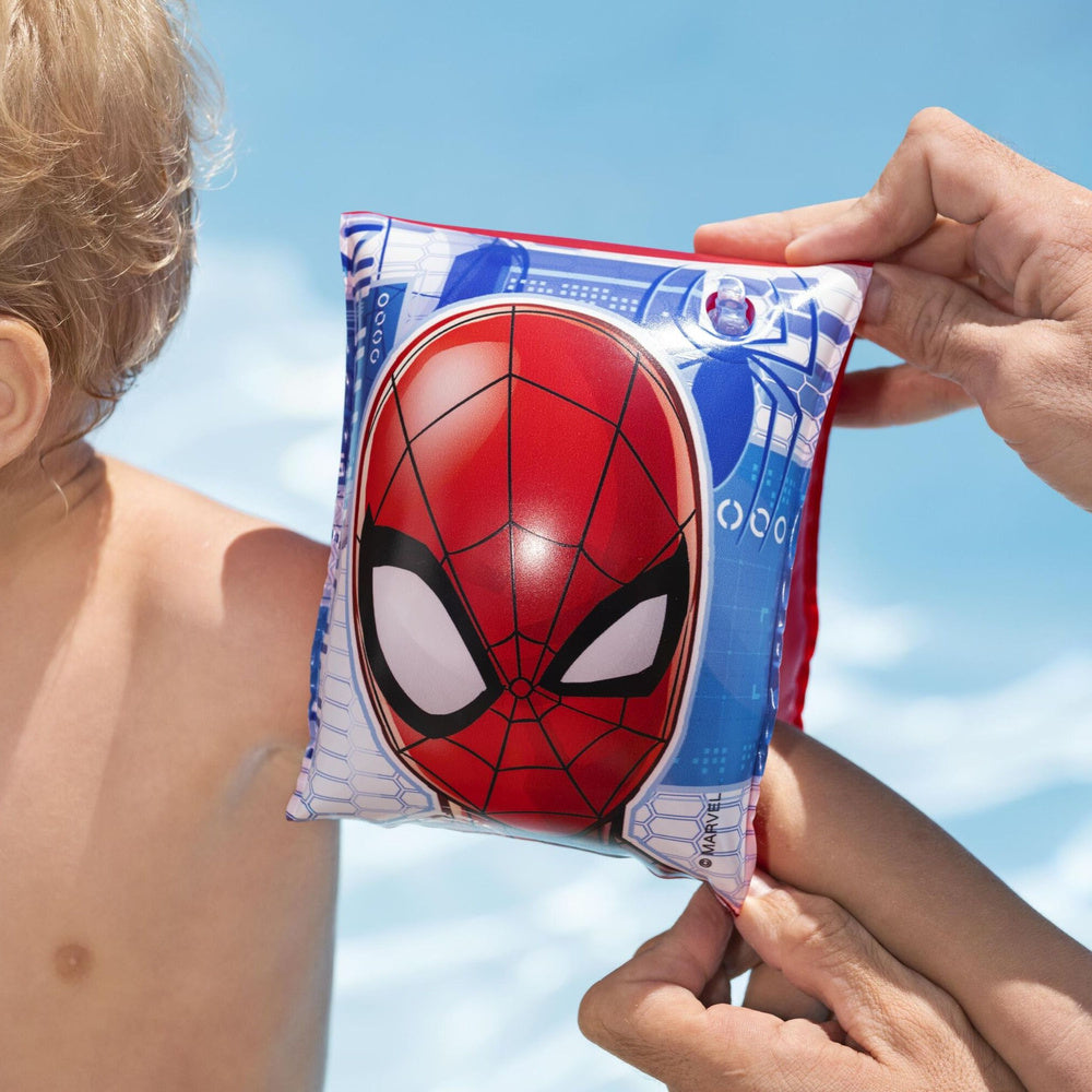 Pieaugušais uzliek bērnam Spider-Man peldēšanas aproci pie baseina vai pludmalē
