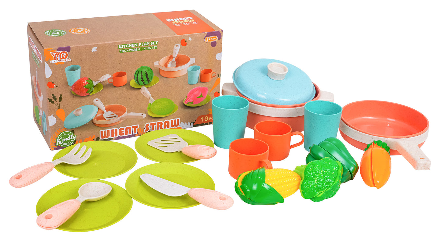 Bērnu Wheat Straw virtuves rotaļu komplekts ar kasti fonā, traukiem, pannām, katlu ar vāku, glāzēm, krūzēm, šķīvjiem, rotaļu dakšiņu, lāpstiņu, nazi un rotaļu dārzeņiem (kukurīza, paprika, burkāns, salātlapa).